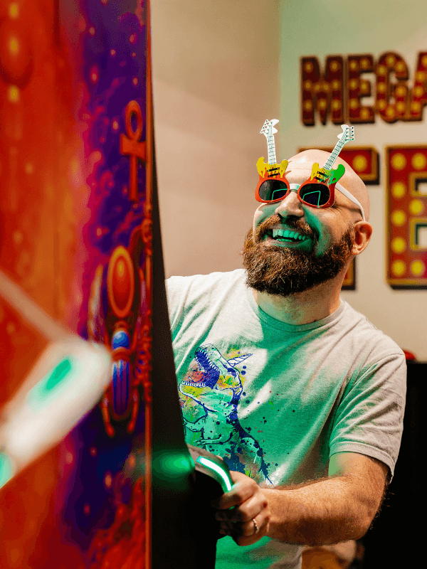 Nos Aventures 2 Participant souriant avec lunettes fantaisie devant une borne de jeu dans l’escape game Las Vegas : Nuit de folie des Secrets du Sablier à Strasbourg.