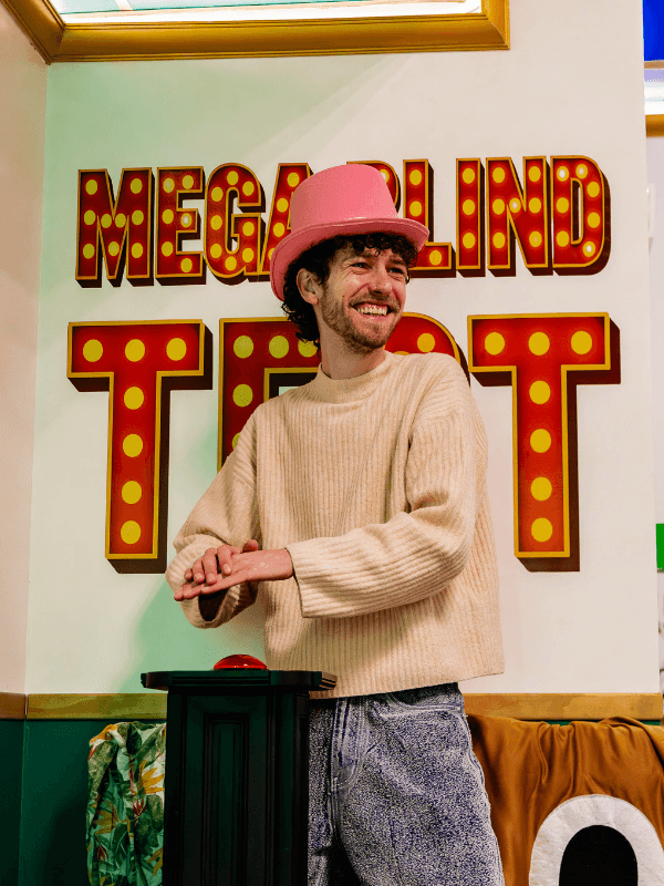 Nos Aventures 3 Joueur avec chapeau rose devant le défi Mega Blind Test dans Las Vegas : Nuit de folie, escape game immersif des Secrets du Sablier à Strasbourg, idéal pour un EVG ou un EVJF.