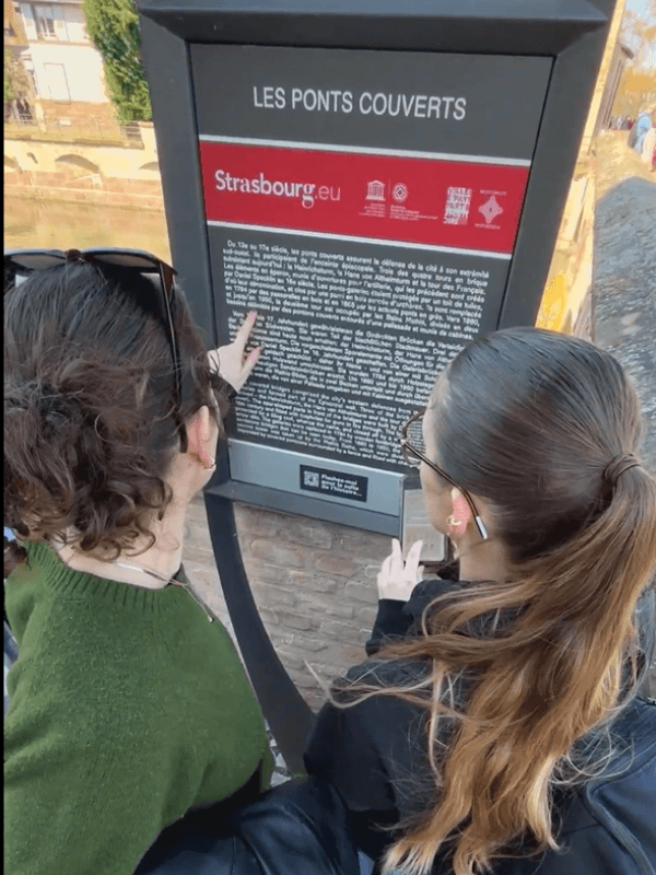 Deux participantes lisant le panneau des Ponts Couverts pendant L’Héritage caché de la Petite France, jeu de piste extérieur sur smartphone des Secrets du Sablier à Strasbourg